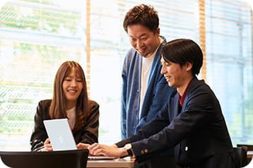 ノートPCを囲んで笑顔で打ち合わせをするPlusAのメンバー